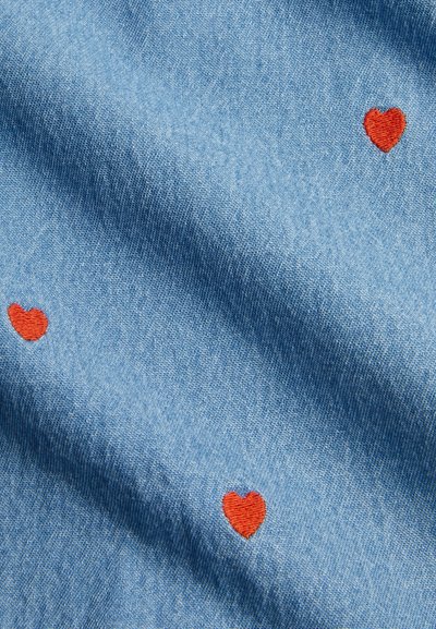 Denim fabric in light blue with several small red embroidered hearts. The texture is smooth with a slight sheen.