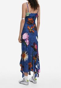 Maxi-mekko kukkakuosilla, sinisestä farkkukankaasta, röyhelökauluksella ja epäsymmetrisellä helmalla. Mallilla on päällään hopeaiset lenkkarit valkoisten sukkien kanssa.