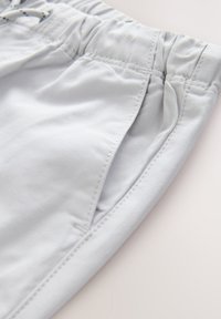 Pantaloni in tessuto grigio chiaro con una fascia elastica in vita e una tasca laterale visibile su uno sfondo semplice.