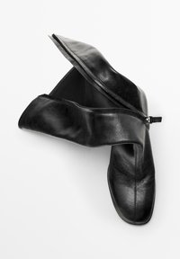 Black leather ankle boots with a zippered opening. Smooth texture and a minimalist design, featuring a pointed toe and low heel.