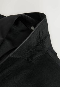 Black garment with a textured wool collar and smooth inner lining, featuring a subtle geometric pattern and contrasting stitching details.