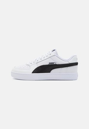 Basket basse blanche Puma avec bande latérale noire et lacets blancs, vue de profil sur fond uni.