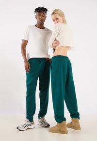 Teal sweatpants with an elastic waistband and side pockets, paired with a light beige cropped sweater. Footwear includes silver sneakers and beige boots.