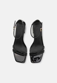 Scarpe open-toe in pelle verniciata nera con punta quadrata, due cinturini incrociati e un cinturino alla caviglia con una chiusura in tono oro.