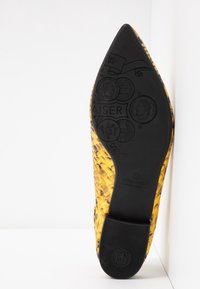 Semelle d'une chaussure pointue jaune à motif peau de serpent avec des pièces embossées et un logo Peter Kaiser sur fond blanc.