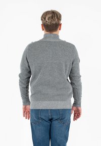 Maglione grigio a maglia con colletto alto, polsini e orlo a coste, abbinato a jeans blu. La texture sembra morbida e calda.