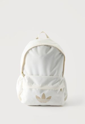 Sac à dos en tissu blanc doux avec poche zippée à l'avant et logo trefoil beige Adidas centré sur la poche sur un fond clair uni.