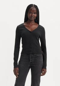 Cardigan noir à rayures côtelées à manches longues avec un col en V, doté d'une fermeture à boutons sur le devant et d'une coupe ajustée, associé à un jean foncé.