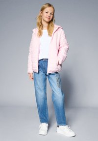 Ljusrosa quiltad jacka med huva, vit t-shirt, ljusblå lösa jeans med mönstrad detalj och vita sneakers.