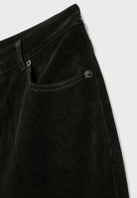 Nærbillede af en lomme på sorte ruskindsbukser med synlig syning og metalnitter på en lys grå baggrund.