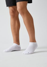 Witte enkelsokken van ademend materiaal, met een mesh-textuur en geribbelde boorden, gecombineerd met zwarte shorts.