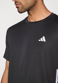 Camiseta deportiva negra de manga corta para hombre con acabado texturizado y un logo triangular blanco en el pecho izquierdo. Diseño de cuello redondo.