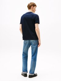 T-shirt di cotone blu navy con collo rotondo, abbinata a jeans dritti azzurri. L'outfit presenta cuciture sottili ai bordi.