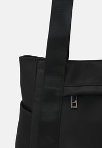 Sac fourre-tout noir en tissu, avec un design structuré, des poignées robustes et un détail de fermeture éclair en métal argenté.