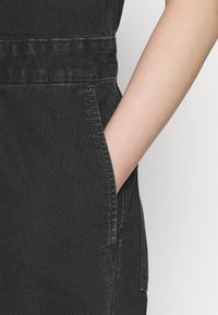 Svarta denimhängselbyxor har en sidoficka med synlig sömnad, som visar upp en jämn textur och en skräddarsydd passform.