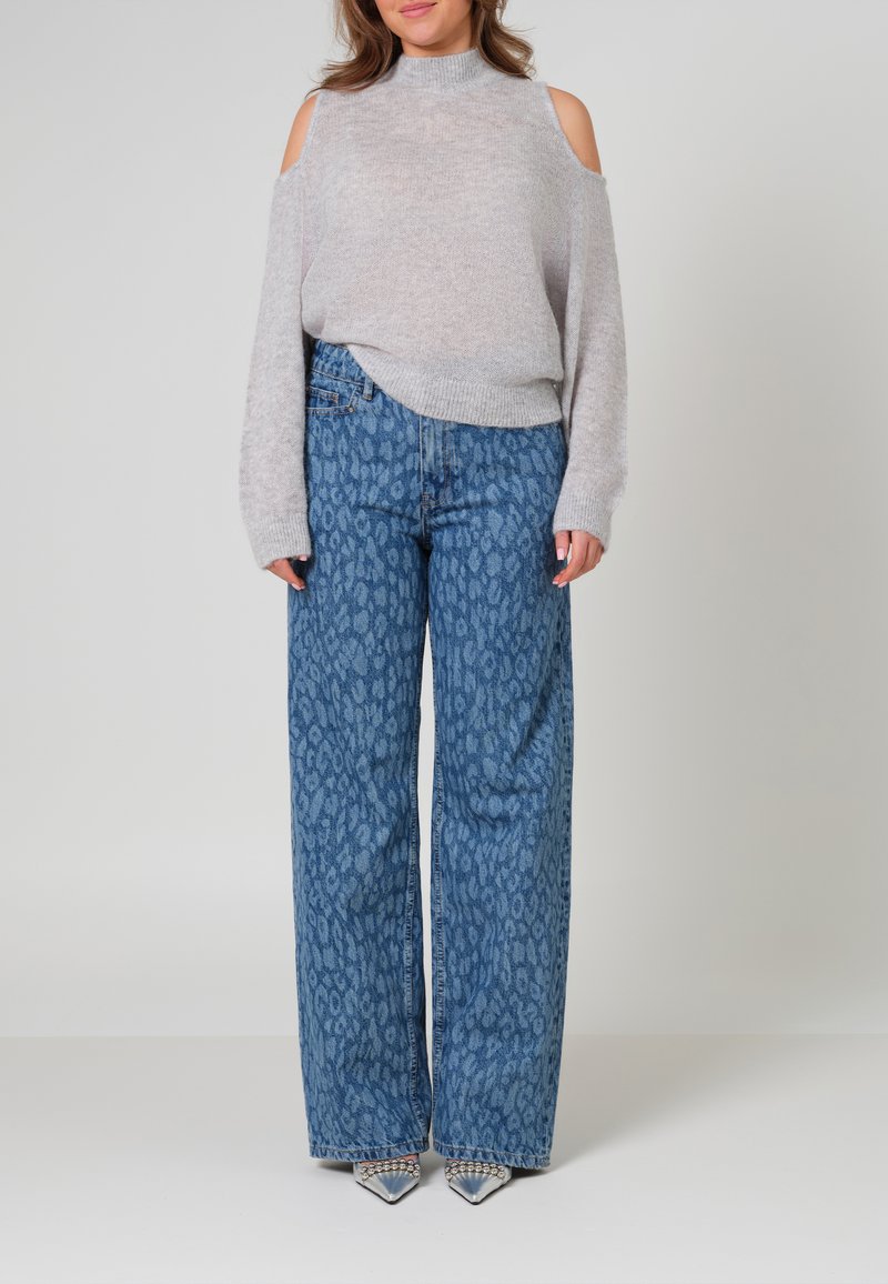 Lichtgrijze, gebreide trui met uitsneden op de schouders, gecombineerd met high-waisted brede broek met een blauw panterprint en metallic puntige hakken.
