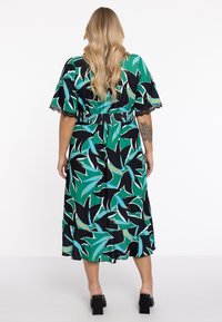 Groene en zwarte bloemenprint jurk met korte mouwen, smocktail, en kantafwerking, ontworpen voor een ontspannen pasvorm. Middenlange zoom.