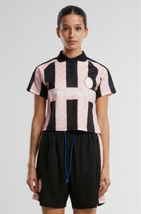 Roza in črna skrajšana polo majica s kratkimi rokavi ima navpične črte, ovratnik z gumbi in logo. Črni kratki hlače z modrim vrvico.