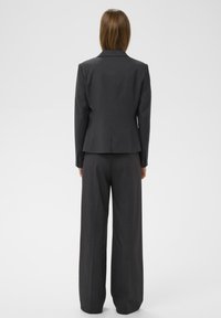 Sötétszürke, testre szabott zakó, strukturált vállakkal és hozzá illő, bőszárú nadrággal. Sima anyag, éles vonalakkal és karcsú sziluettel.