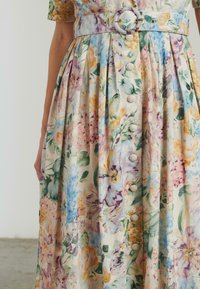 Abito midi a fantasia floreale in tessuto leggero, caratterizzato da tonalità pastello, vita cinquecentesca con una cintura rotonda e bottoni decorativi sul davanti.