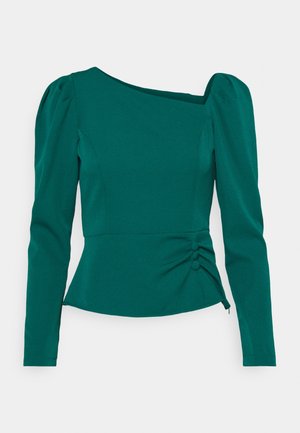 Turkooise groene blouse met lange mouwen, pofschouders, asymmetrische halslijn, getailleerde taille en drie met stof beklede knopen op de zijkant van de plooien.