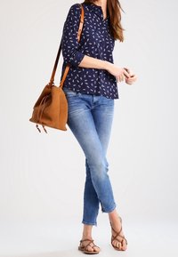 Camisa de marina con patrones blancos, jeans de mezclilla y bolso de ante marrón tipo cubo. Sandalias marrones con tiras entrelazadas.