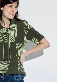 Top a maniche corte in verde oliva con tessuto testurizzato. Presenta un motivo a strisce verdi e un collo a camicia con lacci.