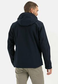 Veste softshell marine avec capuche, présentant une texture lisse, un design ajusté et des coutures contrastantes. Convient pour les activités en extérieur.