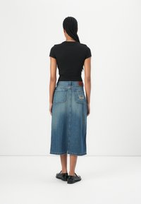 Jeanskjørt med mellomlang lengde, falmet blå farge og to baklommer. Kombinert med en tettsittende svart t-skjorte og svarte sko.