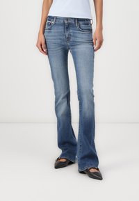 Jeans evazati de culoare albastru închis, din denim spălat mediu, cu ușoară decolorare, talie medie și cinci buzunare, asortați cu balerini negri cu vârful ascuțit.