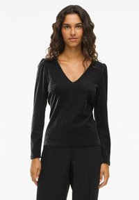 Svart långärmad topp med v-ringning och subtil glans, med samlade axelaccenter och en slät, tight passform.