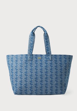 Saco tote em denim azul com padrão geométrico branco, alças duplas de tecido e pequeno logo em destaque. Construção robusta com interior espaçoso.