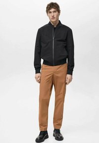 Svart bomberjacka med framdragkedja, ribbade ärmslut och krage; tillsammans med beige chinos i slim fit. Svarta snörskor fullbordar looken.