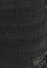 Zbliżenie na czarny dżins z pionowym i poziomym przeszyciem oraz postrzępionymi nitkami w dolnym prawym rogu.