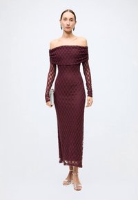 Burgundy off-the-shoulder lace dress with long sleeves, fitted silhouette, and textured pattern, paired with a silver clutch and heels.
