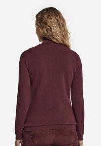 Burgundyröd polotröja i mjukt tyg. Har långa ärmar, ribbade mudd och fåll, med en slät, strukturerad finish.