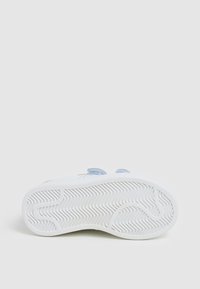 Sneaker bianco con suola in gomma testurizzata, caratterizzata da accenti blu e rossi e strap in velcro. Design pulito con profilo piatto.