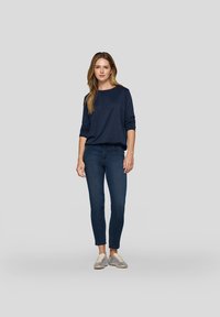 Marineblaue Langarmoberteil, Rundhalsausschnitt, lockere Passform; kombiniert mit dunkelblaus Jeans, taillierte Passform; graue Sneakers mit beigen Schnürsenkeln.