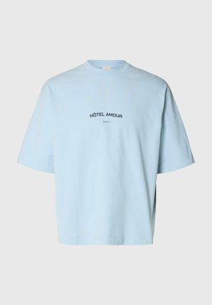 Tricou cu mânecă scurtă de culoare albastru deschis, cu textul „HÔTEL AMOUR” și un mic text „Selected” centrat pe piept, fundal simplu.