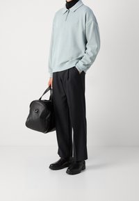 Ljusblå, zippered sweatshirt med krage, parat med svarta byxor. Håller en svart läderväska. Svarta skor med gummisulor.