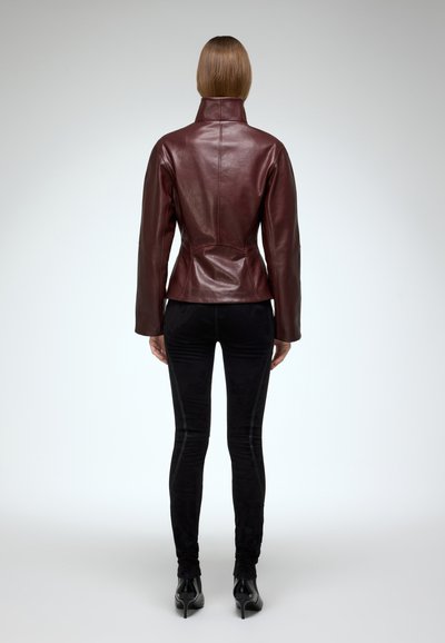 Bordeaux leren jack met een hoge kraag, slim-fit ontwerp en naaddetails, gecombineerd met zwarte fluwelen broek en hoge laarzen.
