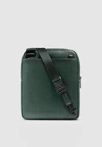 Grüne Ledertasche mit quadratischer Form, verstellbarem schwarzem Riemen und Reißverschluss. Glatte Textur mit minimalen Metallakzenten.