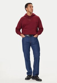 Felpa con cappuccio color mogano con tasca a marsupio, abbinata a jeans blu a gamba dritta. Completata da scarpe nere, creando un look casual.