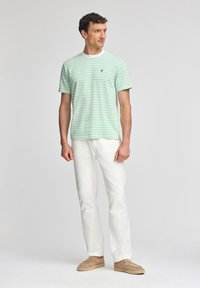 Grönrandig kortärmad t-shirt med vit rund halsringning, kombinerad med vita byxor och beige slip-in skor. Enkel design, lättviktigt material.