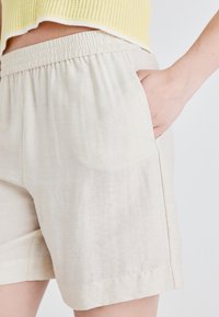Lys beige linshorts med elastisk linning og sidelommer. Stoffet ser ut til å være litt teksturert med en naturlig finish.