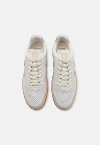 Hvite lær sneakers med perforerte detaljer, beige undertoner, beige snørebånd og en lys brun gummisåle, med en logo på tungen.