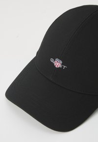 Black baseball cap made of fabric with a structured crown and curved peak, featuring a white embroidered logo on the front.