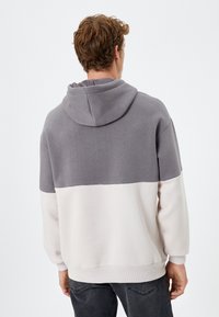 Bluza z kapturem w kolorze szarym i biało-beżowym, wykonana z miękkiego materiału, z prążkowanymi mankietami i dołem.