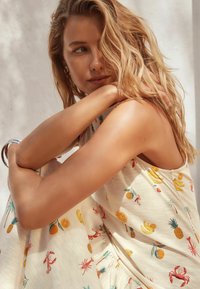 Robe légère sans manches avec un fond crème présentant des imprimés de fruits colorés et de homards. Tissu doux avec un design décontracté et fluide.