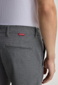 Pantaloni grigi con texture, a taglio dritto, dotati di una tasca posteriore e di un piccolo etichetta rossa "JOOP! JEANS" sulla vita.
